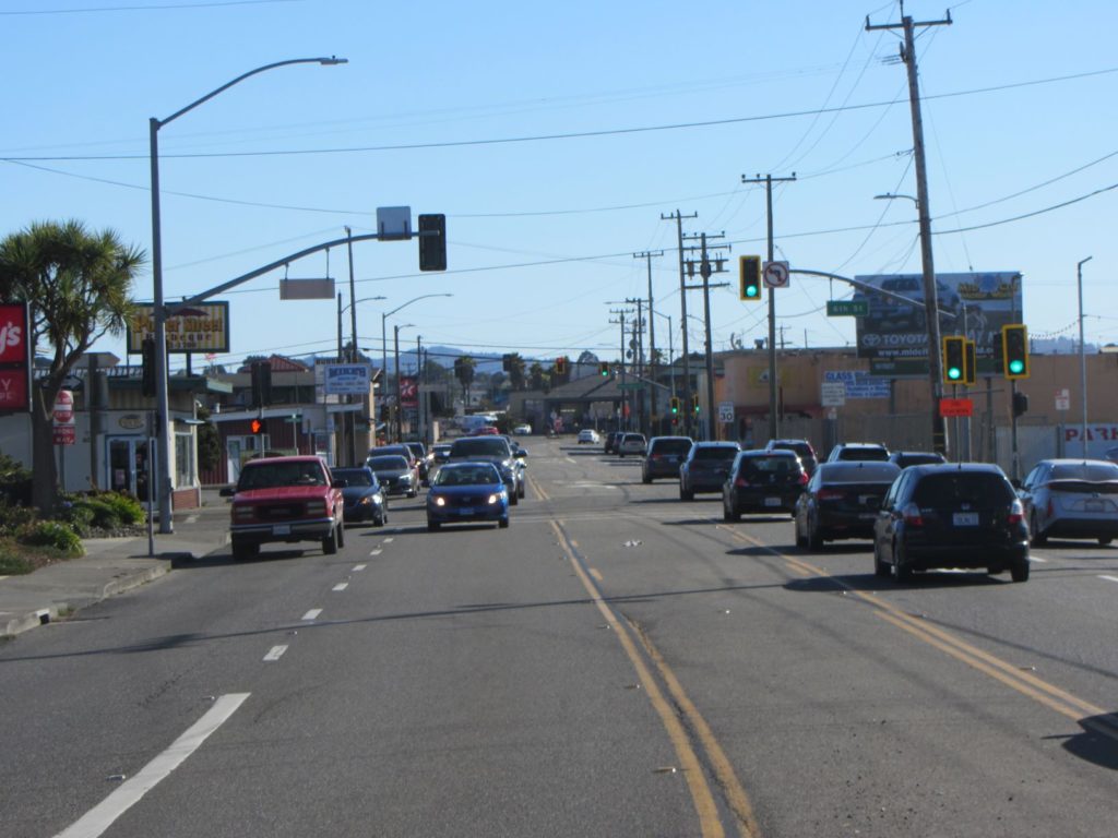 A wide four-lane road with a middle two-way turn lane is filled with cards in both directions.