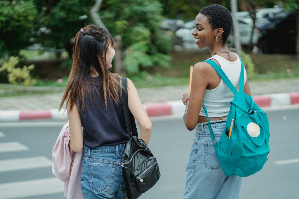 Two young people, seen from behind with backpacks, use a crosswalk and smile at each other