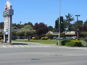 A wide expanse of Central Avenue asphalt is in the foreground, with a parking lot and sign for the McKinleyville Shopping Center behind