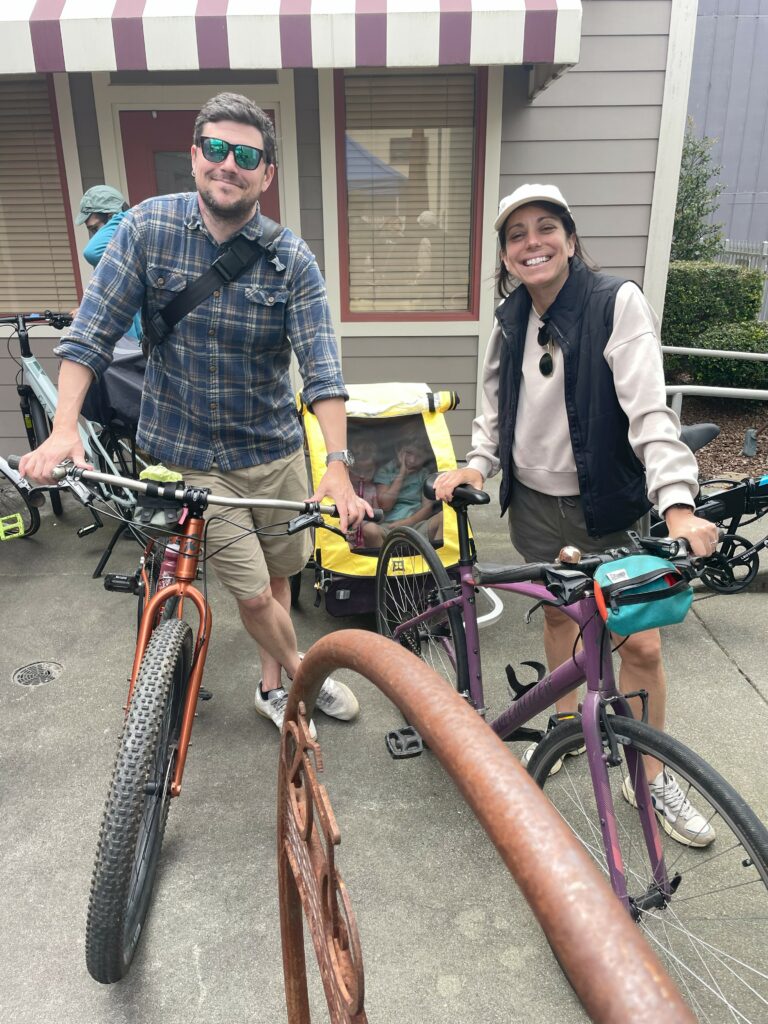 Two people lean on their bikes, one of which has a child trailer attached