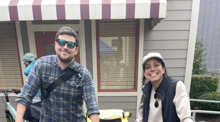 Two people lean on their bikes, one of which has a child trailer attached