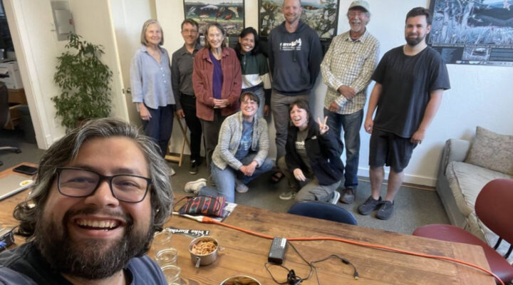 10 people gathered around a table in an office pose for a photo