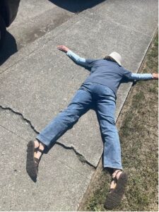 A person is shown lying face down on the sidewalk over a prominent sidewalk crack.