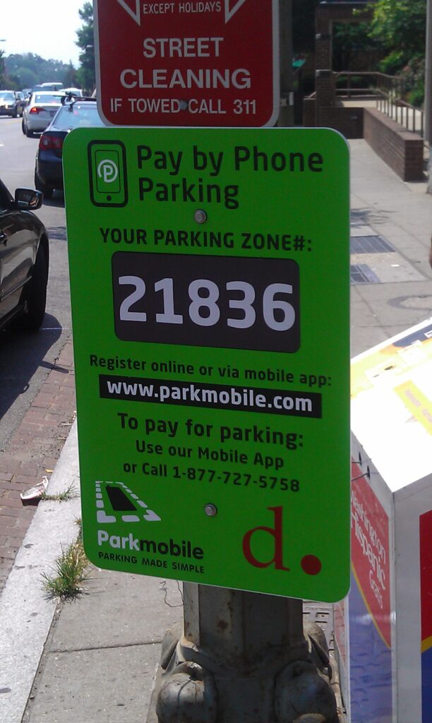 A green sign attached to an existing pole gives directions for paying for parking by phone