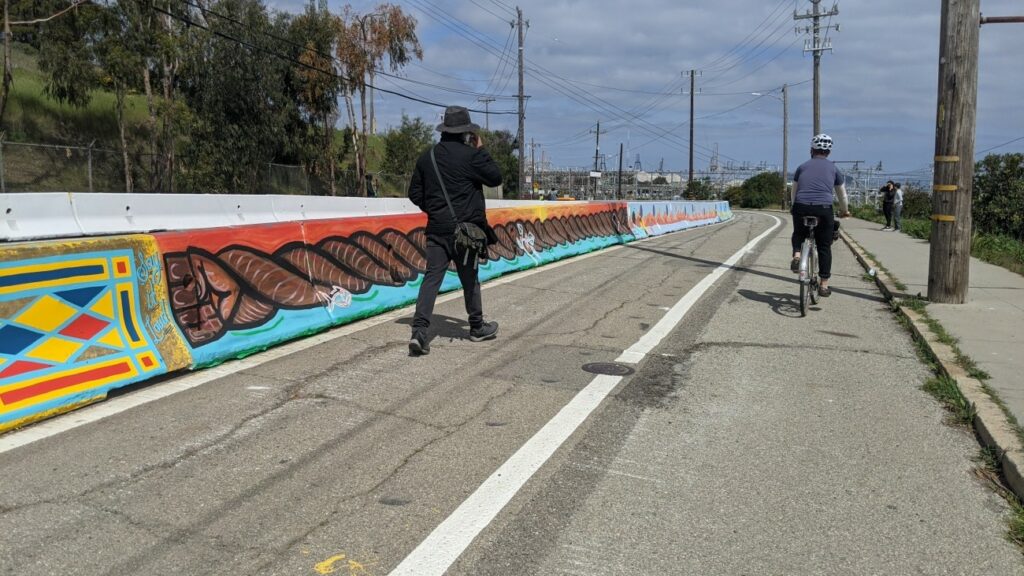 A concrete barrier painted with artistic designs borders a two-lane bike and pedestrian trail