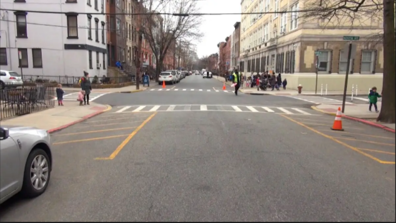 An urban intersection with yellow striped paint prohibiting parking on either side of the street near the corner