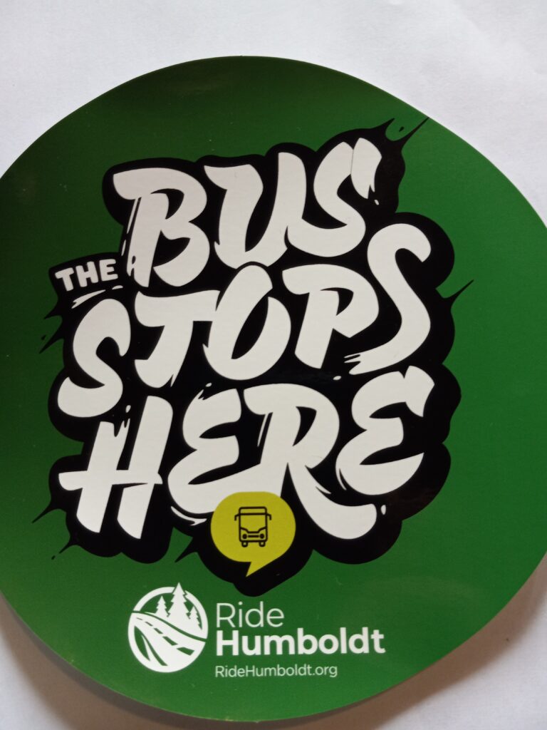 A circular green sticker on a white background reads "The Bus Stops Here" in stylized font.