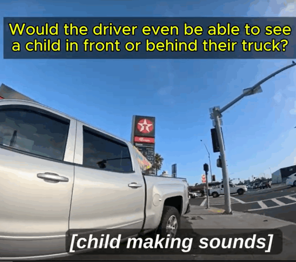 A video screen shot shows a pickup truck looming large next to a sidewalk, with an intersection and traffic light visible in the background. Text reads "Would the driver even e able to see the child in front of or behind their truck?" and a caption says "[child making sounds]".