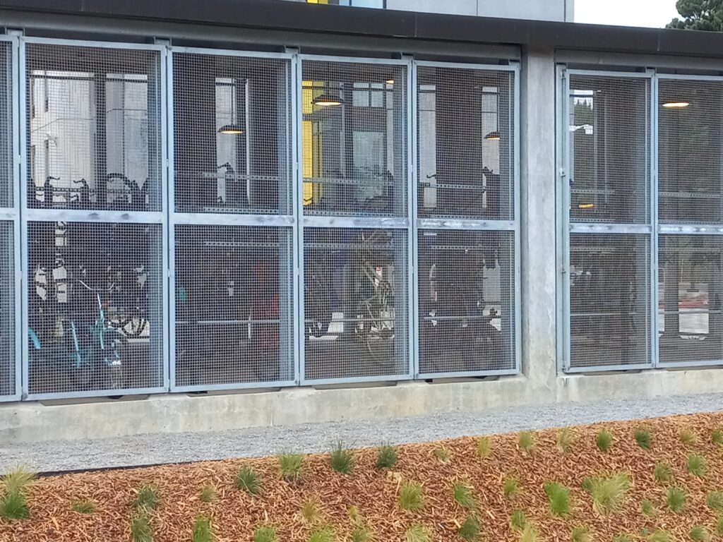 A roofed structure with metal grate walls is seen from the outside. Bicycles can be seen stores inside.