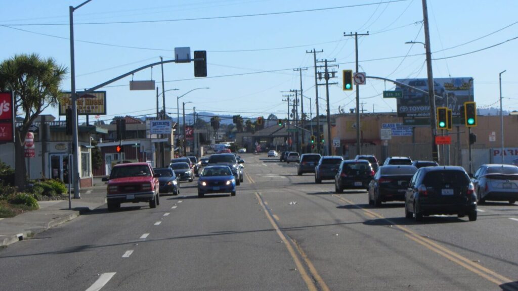 A wide four-lane road with a middle two-way turn lane is filled with cards in both directions.