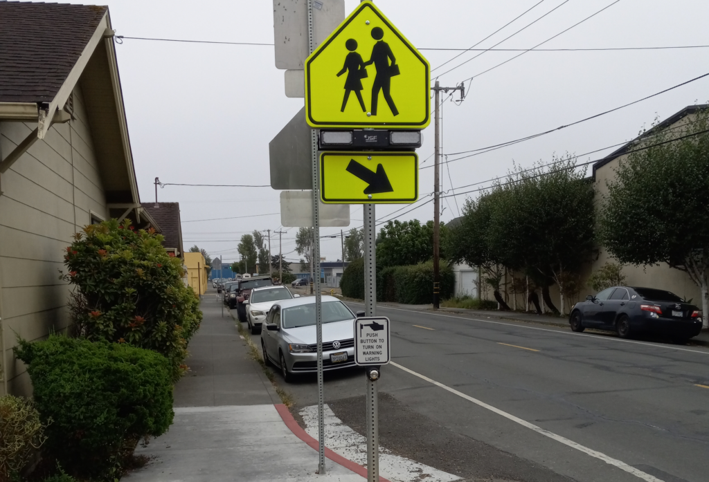 A yellow pedestrian warning sign with flashing lights at the corner of K and 8th Streets in Arcata