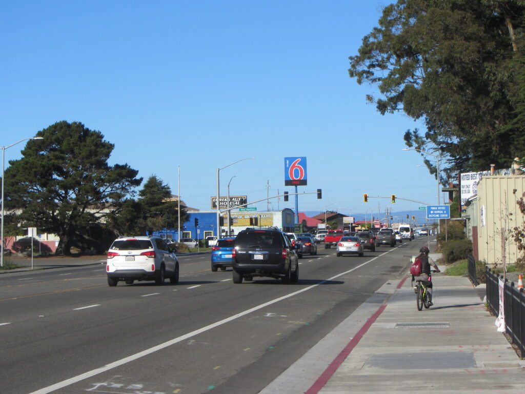 A bicyclist on a sidewalk next to a busy street.