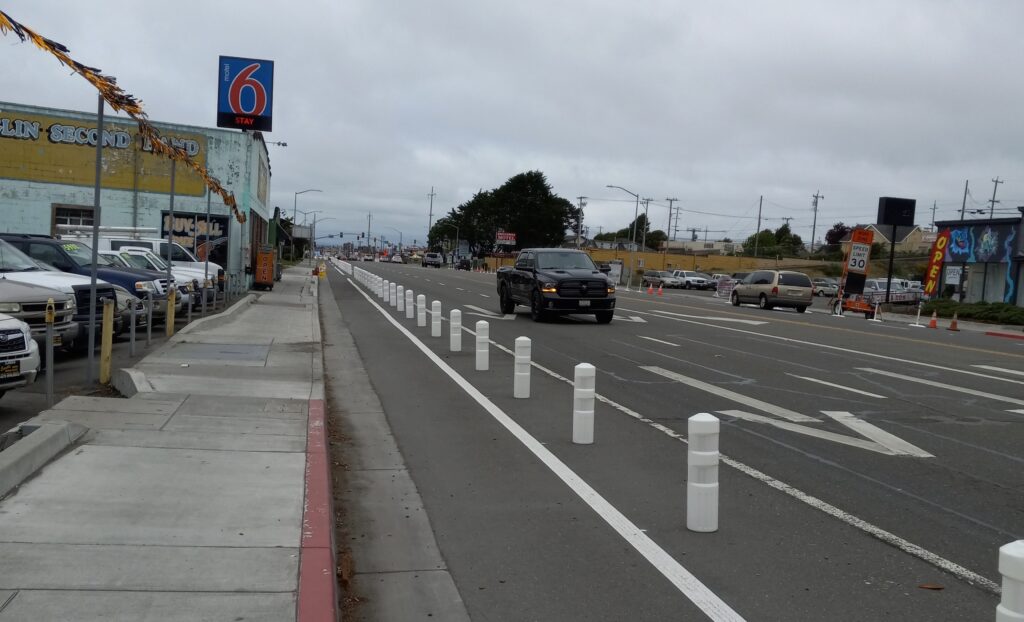 Plastic bollards between a bike lane and a wide street.