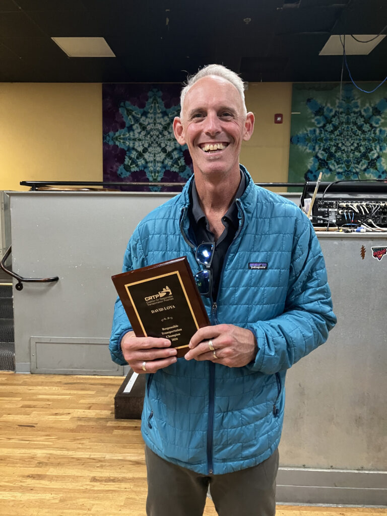 A white man with gray hair wearing a blue jacket and holding a plaque